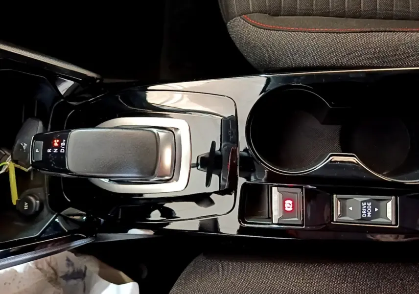 Vue rapprochée de la console centrale noire brillante avec levier de vitesse automatique et boutons Drive Mode et frein à main électrique d'une Peugeot 208 blanche.
