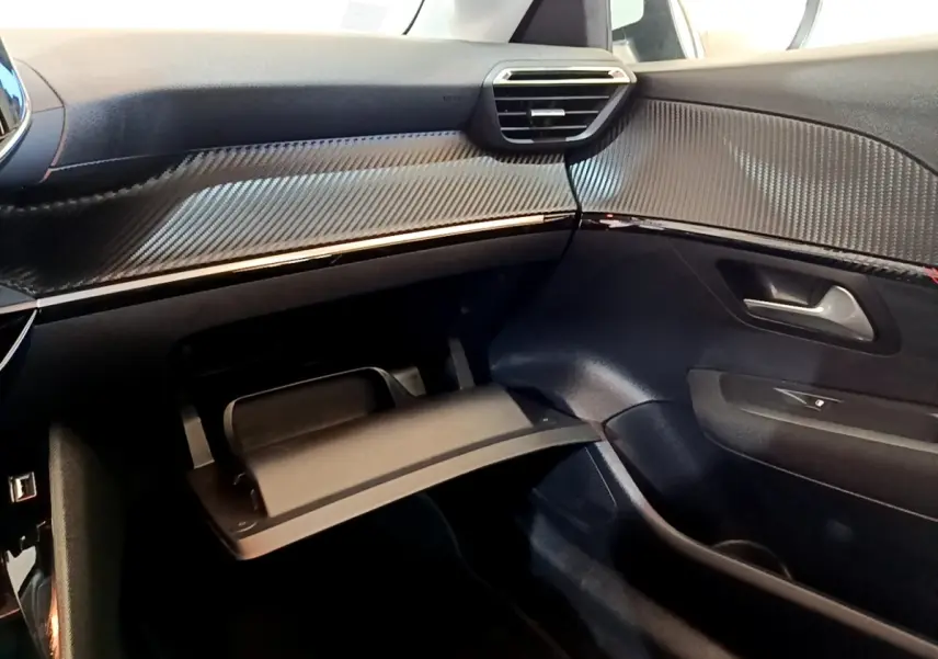 Vue intérieure côté passager du tableau de bord noir et boîte à gants ouverte d'une Peugeot 208 Electrique blanche.