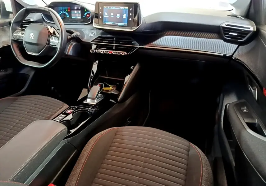 Intérieur de la Peugeot 208 électrique blanc, vue côté conducteur, tableau de bord moderne avec écran tactile central.