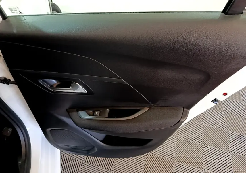 Vue rapprochée de la porte arrière droite noire avec poignée intérieure argentée d’une Peugeot 208 électrique blanche.