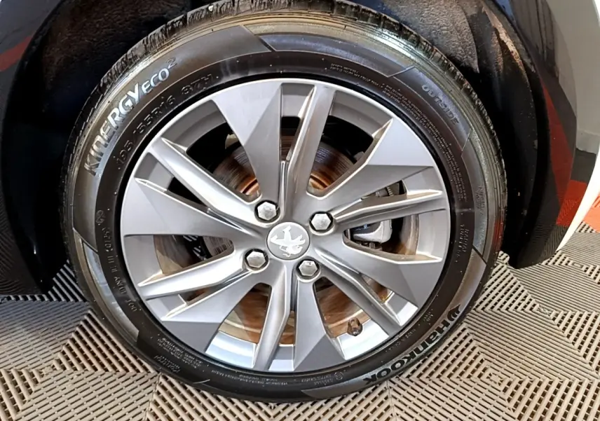 Gros plan sur la roue avant droite avec jante argentée et pneu Hankook d'une Peugeot 208 blanche électrique.