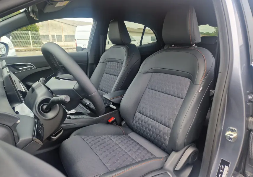 Vue intérieure côté conducteur du MG3 1.5L HYBRID+ 195CH Luxury 2026 en gris Hampstead, sièges tissu et cuir noir avec surpiqûres orange.
