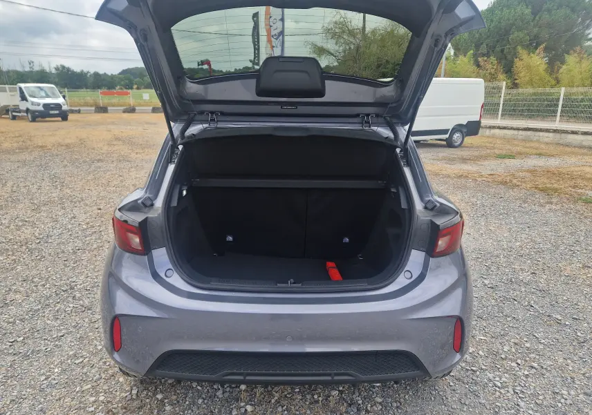 Vue arrière du coffre ouvert de la MG3 1.5L HYBRID+ 195CH Luxury en gris Hampstead, sur un sol gravillonné.