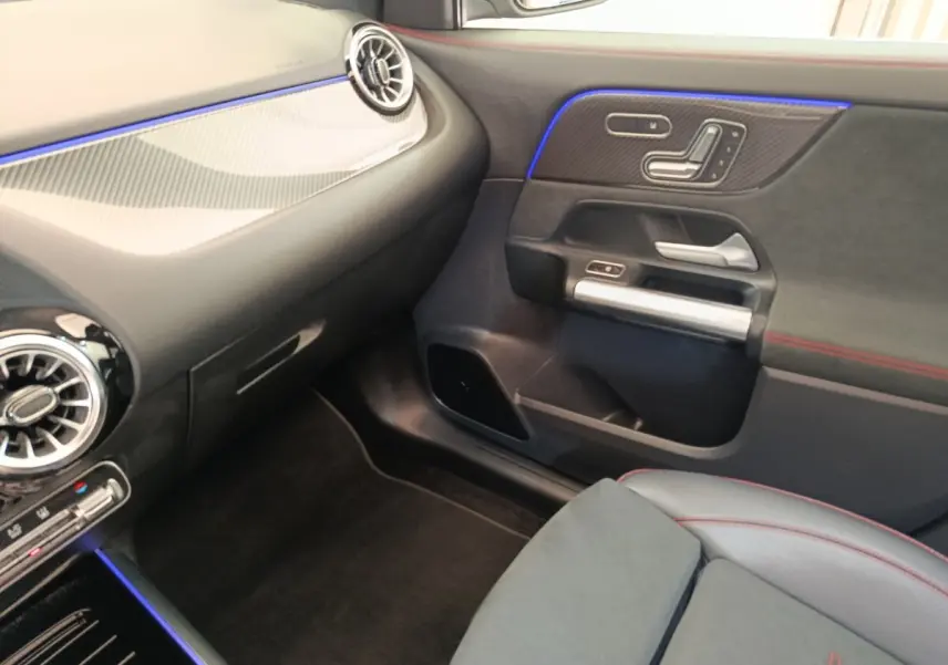 Intérieur côté passager d'une Mercedes GLA 250 e AMG Line 2021, avec éclairage d'ambiance bleu et surpiqûres rouges.