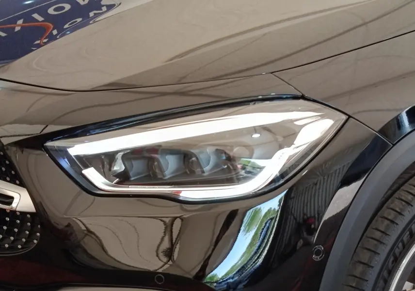 Gros plan sur le phare avant droit LED d’une Mercedes GLA 250 e AMG Line noire, avec partie de la calandre visible.