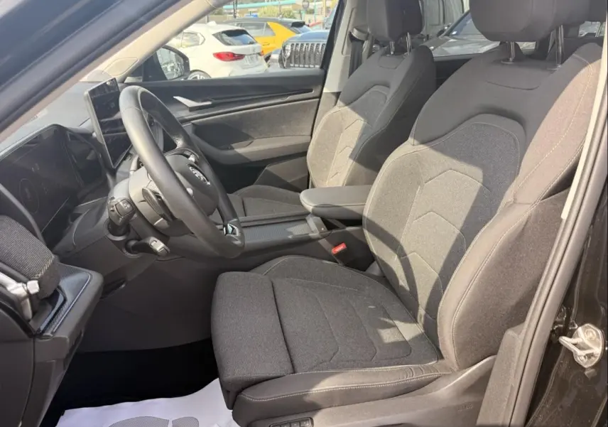 Intérieur avant droit du Skoda Kodiaq 2024 noir, sièges tissu gris et tableau de bord avec écran tactile.