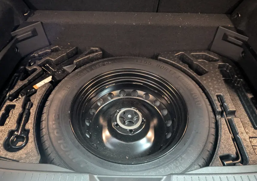 Vue rapprochée de la roue de secours noire et des outils de bord dans le coffre du Nissan Qashqai blanc 2024.
