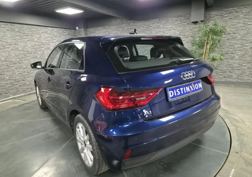 Audi A1 Sportback bleu métallisé vue 3/4 arrière droit avec feux LED et toit contrasté en intérieur showroom.