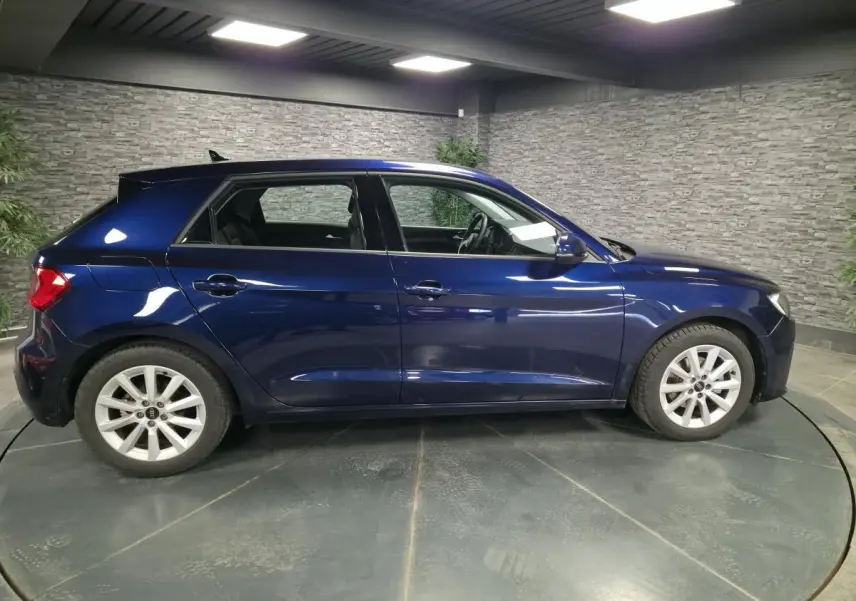 Audi A1 Sportback bleu métallisé vue de profil côté gauche dans un showroom avec mur en pierre grise.
