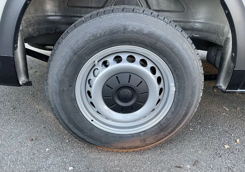 Gros plan sur la roue arrière droite du Volkswagen Crafter Van noir intense, jante acier grise avec logo VW au centre.