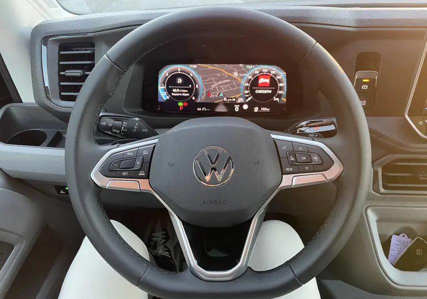 Vue rapprochée du volant noir du Volkswagen Crafter 2025 avec tableau de bord numérique et commandes intégrées.
