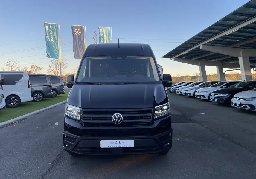 Vue frontale d'un Volkswagen Crafter Van noir intense 2025 avec phares LED et calandre noire sur parking.