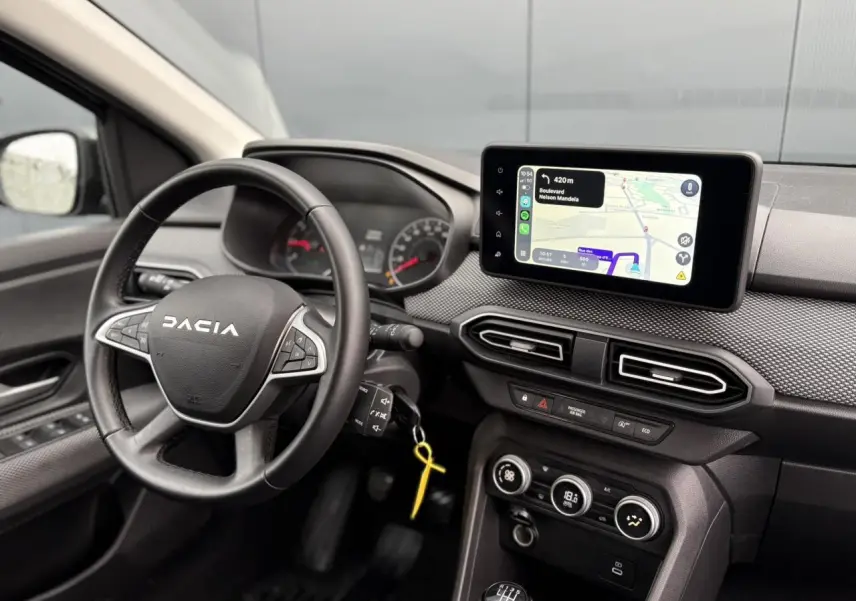 Vue intérieure du tableau de bord du Dacia Jogger 2025, avec volant noir, écran tactile GPS et commandes intégrées.