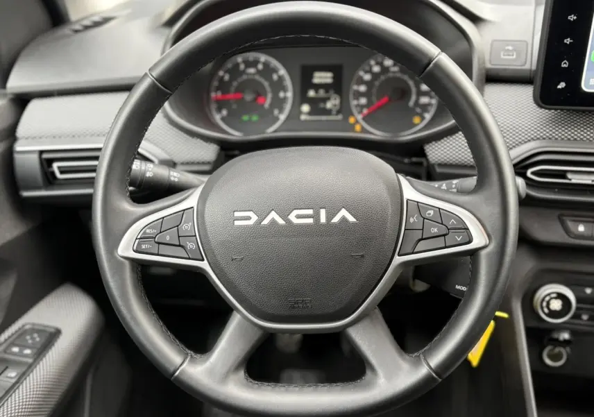 Vue rapprochée du volant noir DACIA JOGGER 2025 avec commandes intégrées et tableau de bord en arrière-plan.