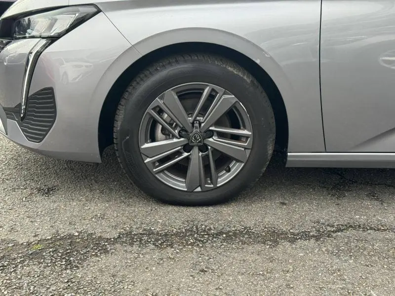 Gros plan sur la roue avant gauche et partie du pare-chocs d'une Peugeot 308 2024 gris Artense avec jante alliage distinctive.