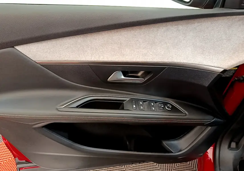 Vue intérieure de la porte avant gauche rouge du Peugeot 3008 GT 2021 avec commandes de vitres et poignée argentée.