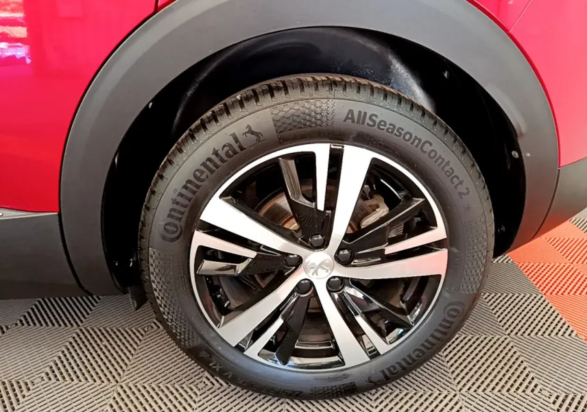 Gros plan sur la roue avant droite d’un Peugeot 3008 rouge, mettant en valeur la jante alliage bicolore et le pneu Continental.