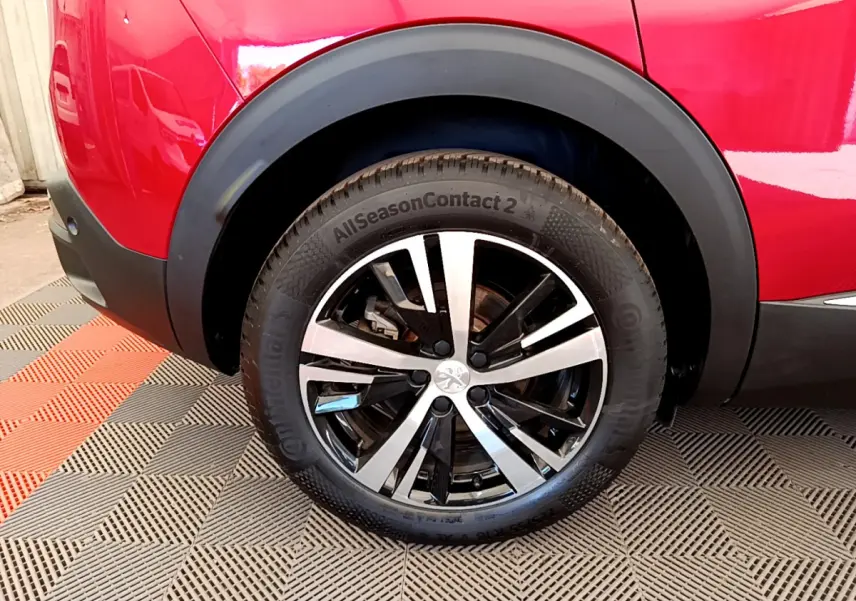 Gros plan sur la roue arrière droite du Peugeot 3008 rouge, avec jante alliage bicolore et pneu toutes saisons.