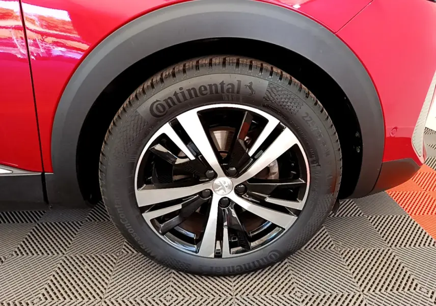 Gros plan sur la roue avant gauche d’un Peugeot 3008 rouge, avec jante alliage bicolore et pneu Continental.