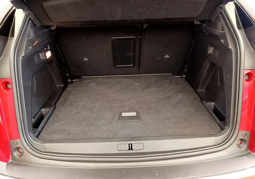 Coffre ouvert vu de l'arrière d'un Peugeot 3008 rouge, montrant un espace de chargement propre et bien fini.