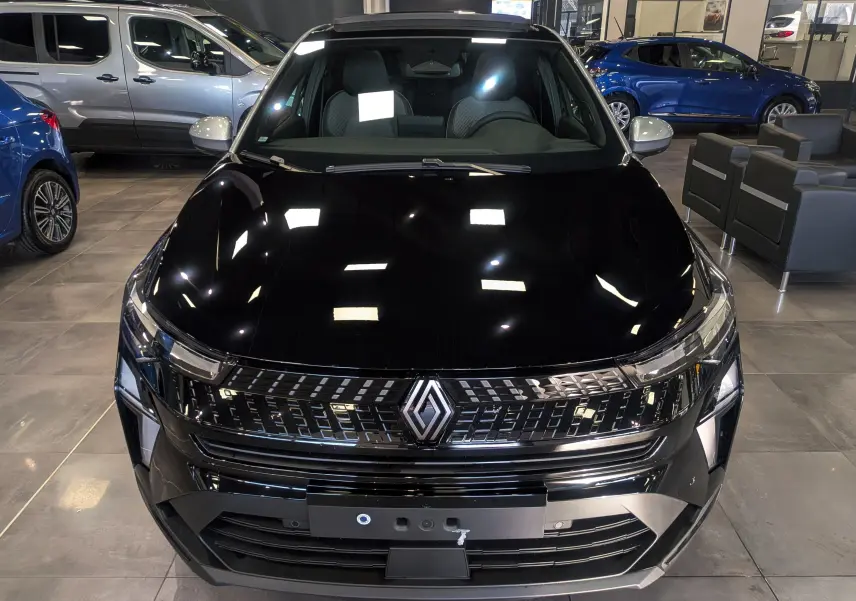 Vue avant d’un Renault Captur E-TECH Full Hybrid noir avec toit gris Highland, en showroom, mettant en valeur sa calandre moderne.