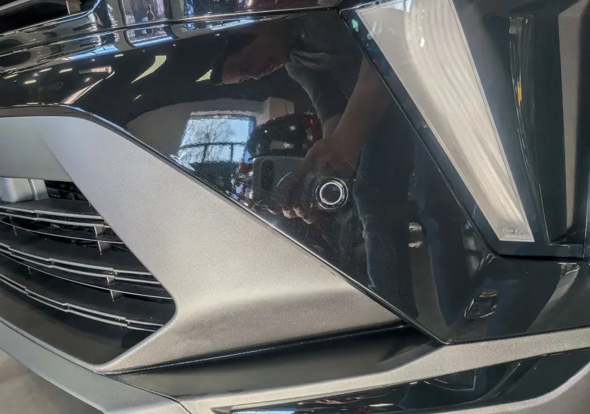 Gros plan sur le pare-chocs avant noir du Renault Captur E-TECH avec capteur de stationnement circulaire visible.