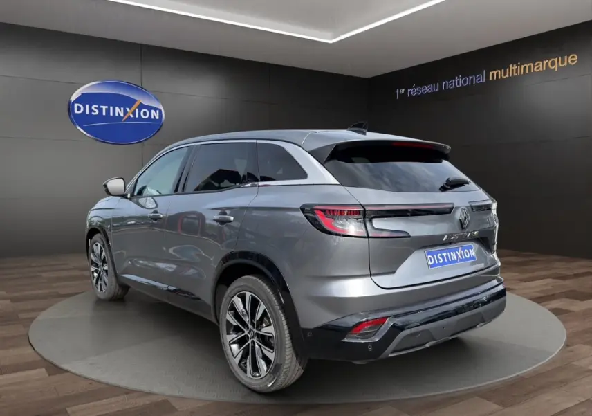 Vue 3/4 arrière droite du Renault Austral Techno E-Tech gris foncé avec feux LED et toit spoiler en intérieur showroom.