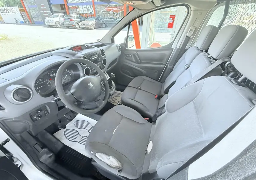 Vue intérieure côté conducteur du Peugeot Partner blanc 2014, montrant le volant, la boîte manuelle et les sièges usés.