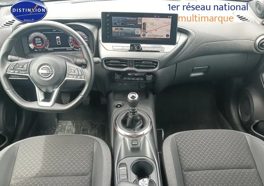 Intérieur de Nissan Juke 2025 vue avant, tableau de bord noir avec écran tactile et levier de vitesses manuel.