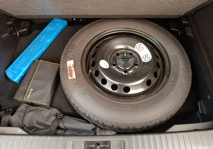 Vue plongeante sur la roue de secours noire et les accessoires dans le coffre du Renault Captur gris clair 2022.