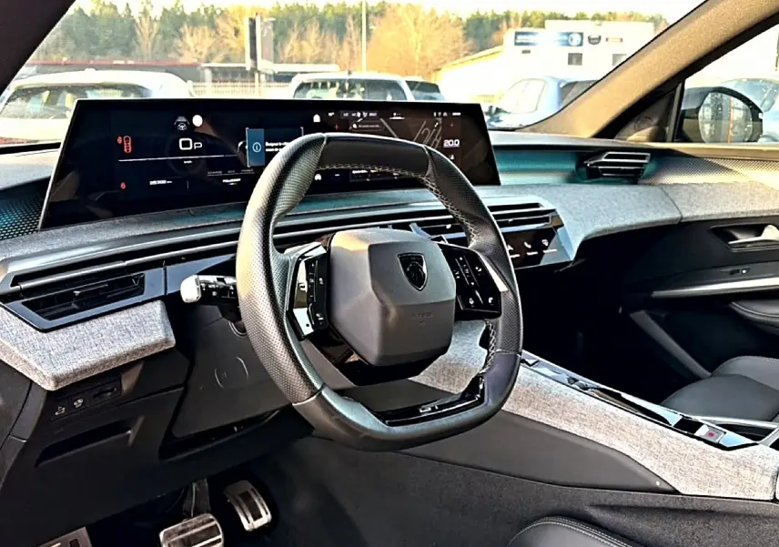 Vue intérieure avant du Peugeot 3008 gris 2025, volant cuir multifonction et tableau de bord numérique large.