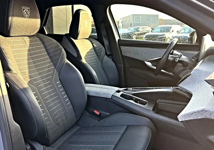 Vue intérieure côté conducteur du Peugeot 3008 gris 2025, sièges en tissu et cuir avec logo Peugeot brodé.