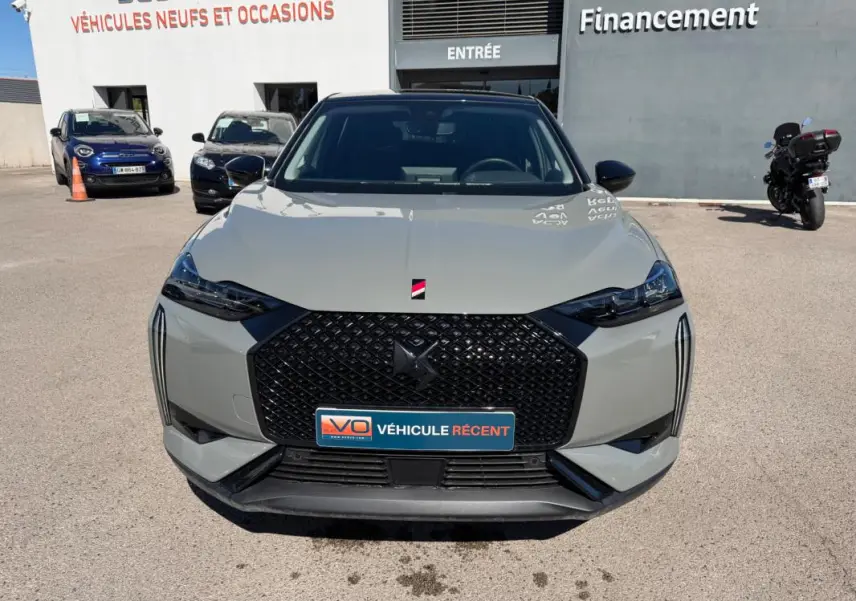 Vue de face d'une DS3 100 BVM6 Performance Line gris 2024 avec calandre noire et phares effilés, sur parking extérieur.