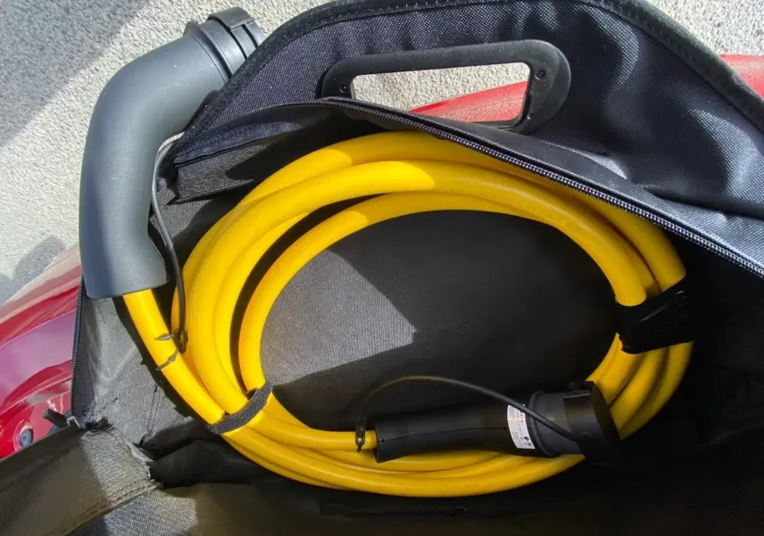 Câble de recharge jaune enroulé dans un sac noir posé sur le coffre rouge d'une Fiat 500 Cabriolet Electrique.