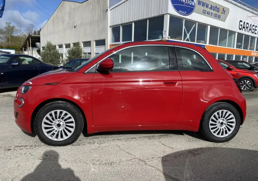 Profil latéral gauche d'une FIAT 500 Cabriolet Electrique rouge stationnée devant un garage avec jantes alliage 16 pouces.