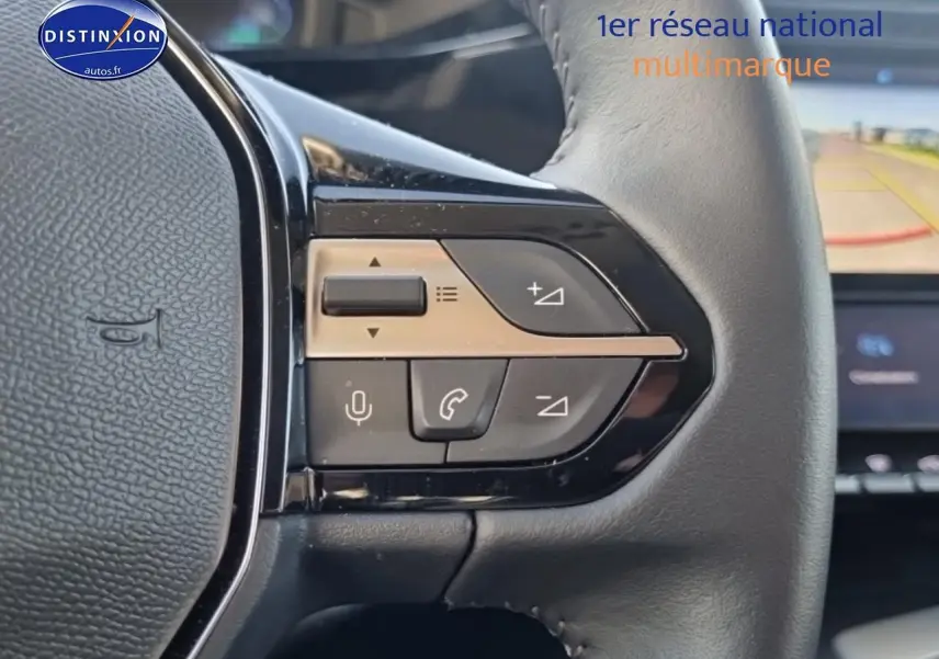 Gros plan sur les commandes du volant cuir noir de la Peugeot 408 Hybrid 145 allure e-dcs6, avec écran tactile en arrière-plan.