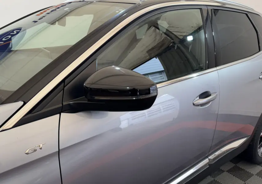 Vue latérale côté gauche d’un Peugeot 3008 GT gris clair avec rétroviseur noir brillant et badge GT visible.