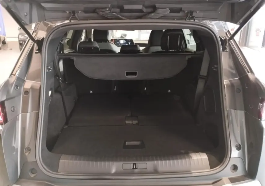 Coffre ouvert vu de l'arrière d'un Peugeot 5008 gris titanium, banquettes arrière rabattues et cache-bagages déployé.