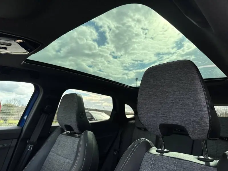 Vue intérieure du Renault Austral 2025, toit panoramique et sièges gris avec surpiqûres noires visibles côté gauche.