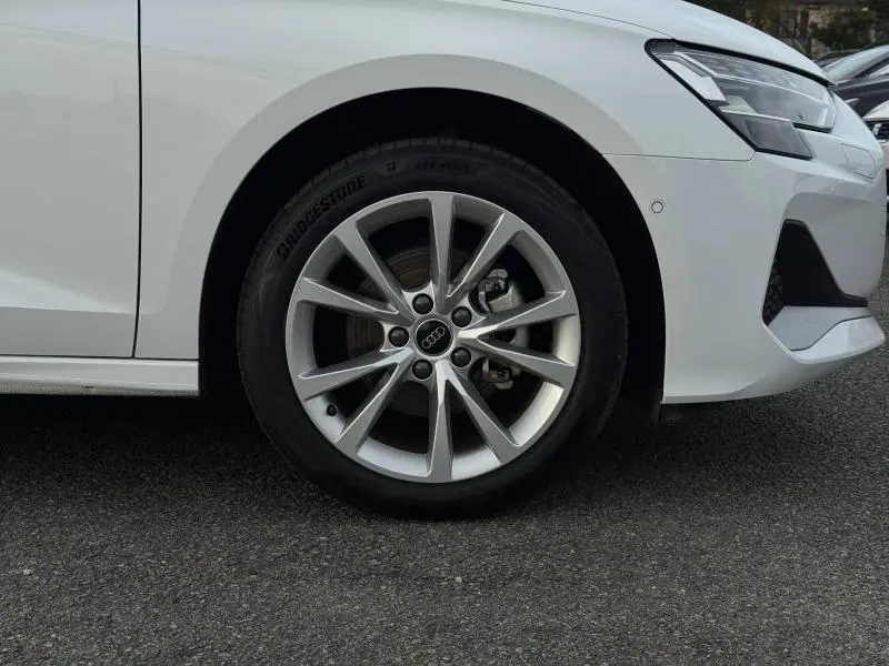 Gros plan sur la roue avant gauche et partie du pare-chocs blanc d’une Audi A3 Sportback 30 TFSI Hybride 2024.