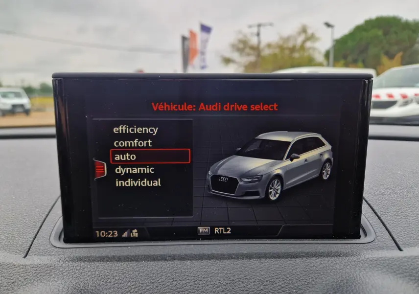 Écran intérieur montrant le mode Audi drive select avec une voiture grise vue en 3/4 avant droite.