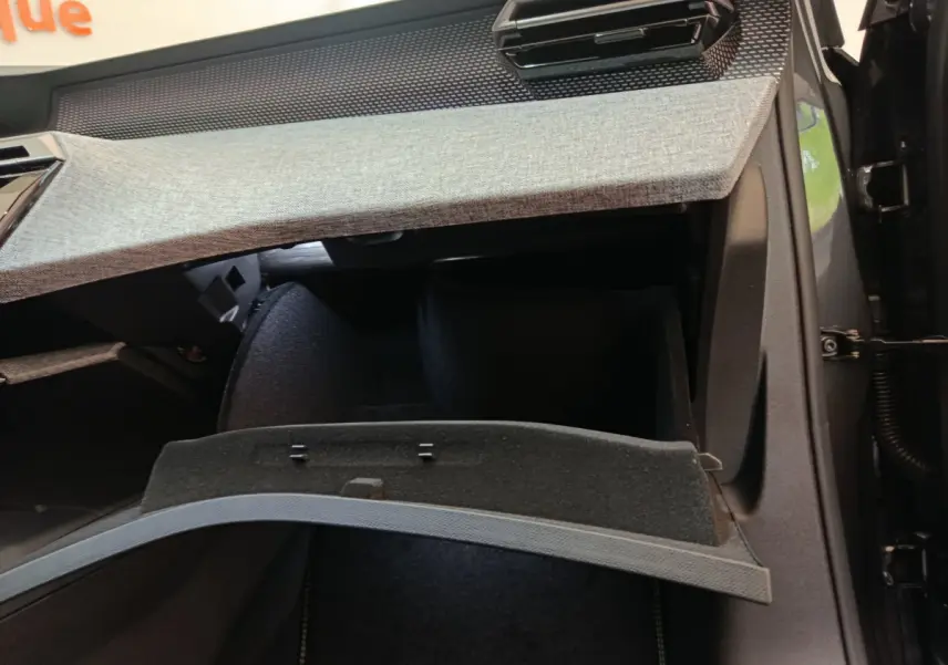 Intérieur du Peugeot 3008 2025 noir, vue sur la boîte à gants ouverte avec tableau de bord gris clair texturé.