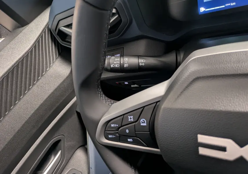 Vue rapprochée du volant noir du Dacia Duster Hybrid 140 Journey 2025, montrant les commandes au volant et la manette des phares.