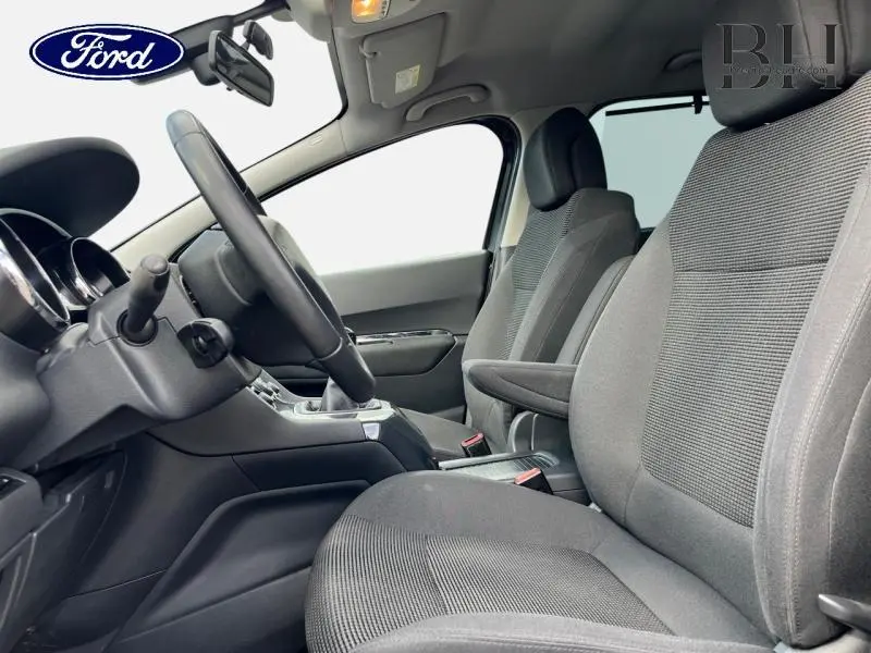 Vue intérieure côté conducteur d'un Ford avec sièges tissu gris et volant noir, tableau de bord partiellement visible.