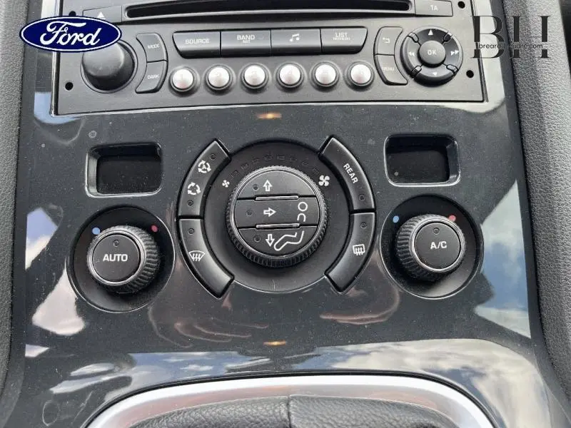 Panneau de commande de climatisation noir brillant avec boutons ronds et molette centrale dans un Peugeot 5008 noir Perla Nera.