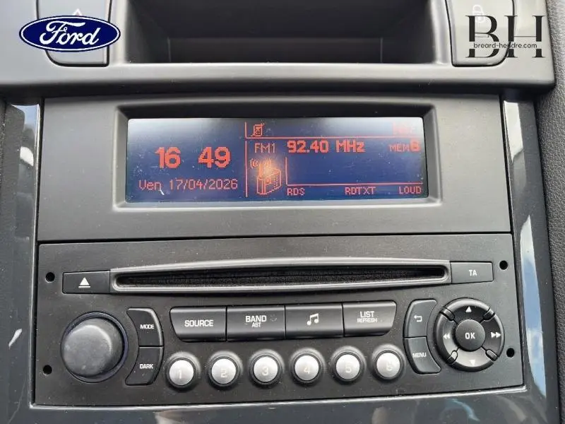 Vue rapprochée de la radio CD MP3 intégrée au tableau de bord noir du Peugeot 5008, affichage digital orange.