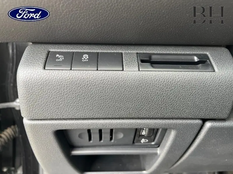 Gros plan sur les commandes intérieures grises d’un véhicule Ford, avec boutons de désactivation et fente de carte.