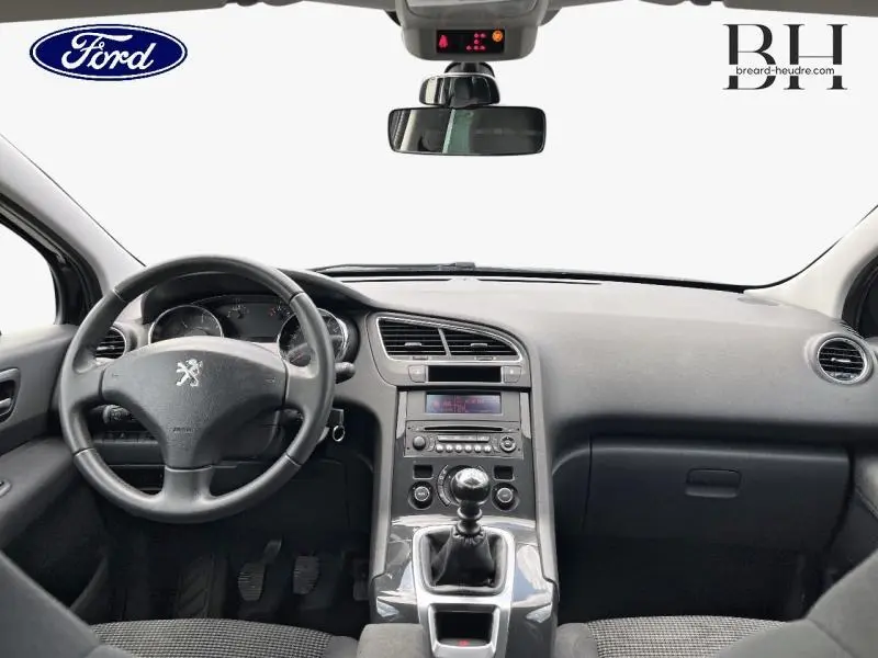 Vue intérieure avant du Peugeot 5008 noir Perla Nera, montrant le volant cuir, tableau de bord et levier de vitesse manuel.