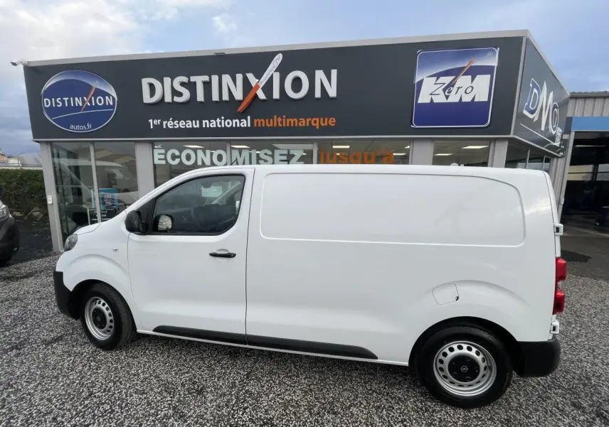 Vue de profil côté gauche d'un utilitaire Opel Vivaro blanc stationné devant un concessionnaire multimarque.