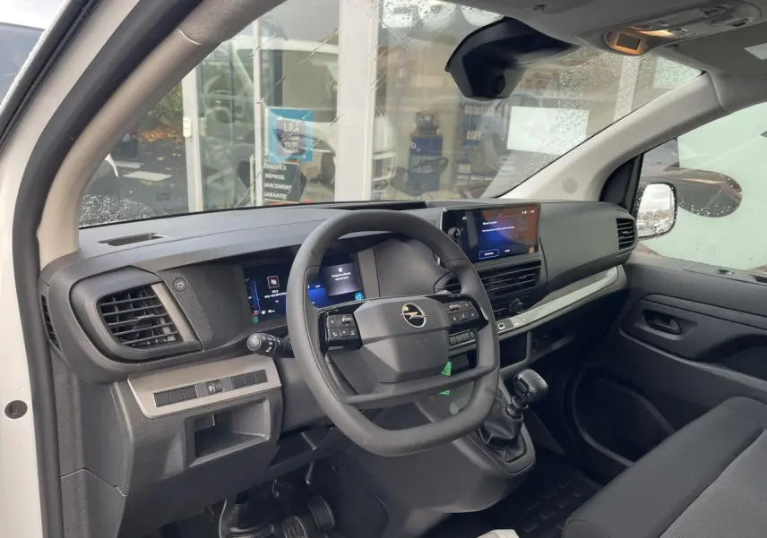 Intérieur avant droit de l'Opel Vivaro blanc 2024, volant multifonction, écran tactile et levier de vitesses manuel visibles.